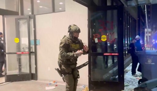 A masked ICE fed fumbles with the pin of a smoke/tear gas grenade while having his shotgun held BETWEEN HIS KNEES pointing upward like a strap-on ignoring all rules of gun safety