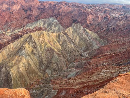 An almost top-down view of the anticline within its large crater of red rock. Steep slopes and contours may be seen all along the dome.