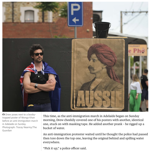 An image and then article text. The image is captioned: Drew poses next to a booby-trapped poster of Monga Khan before an anti-immigration march in Adelaide on Sunday. The article continues: This time, as the anti-immigration march in Adelaide began on Sunday morning, Drew cheekily covered one of his posters with another, identical one, stuck on with masking tape. He added another prank – he rigged up a bucket of water.  An anti-immigration protester waited until he thought the police had passed then tore down the top one, leaving the original behind and spilling water everywhere.  “Pick it up,” a police officer said.  The officer and his colleagues waited, and watched, until the protester put every last scrap in a bin. “Good boy,” one of them said.